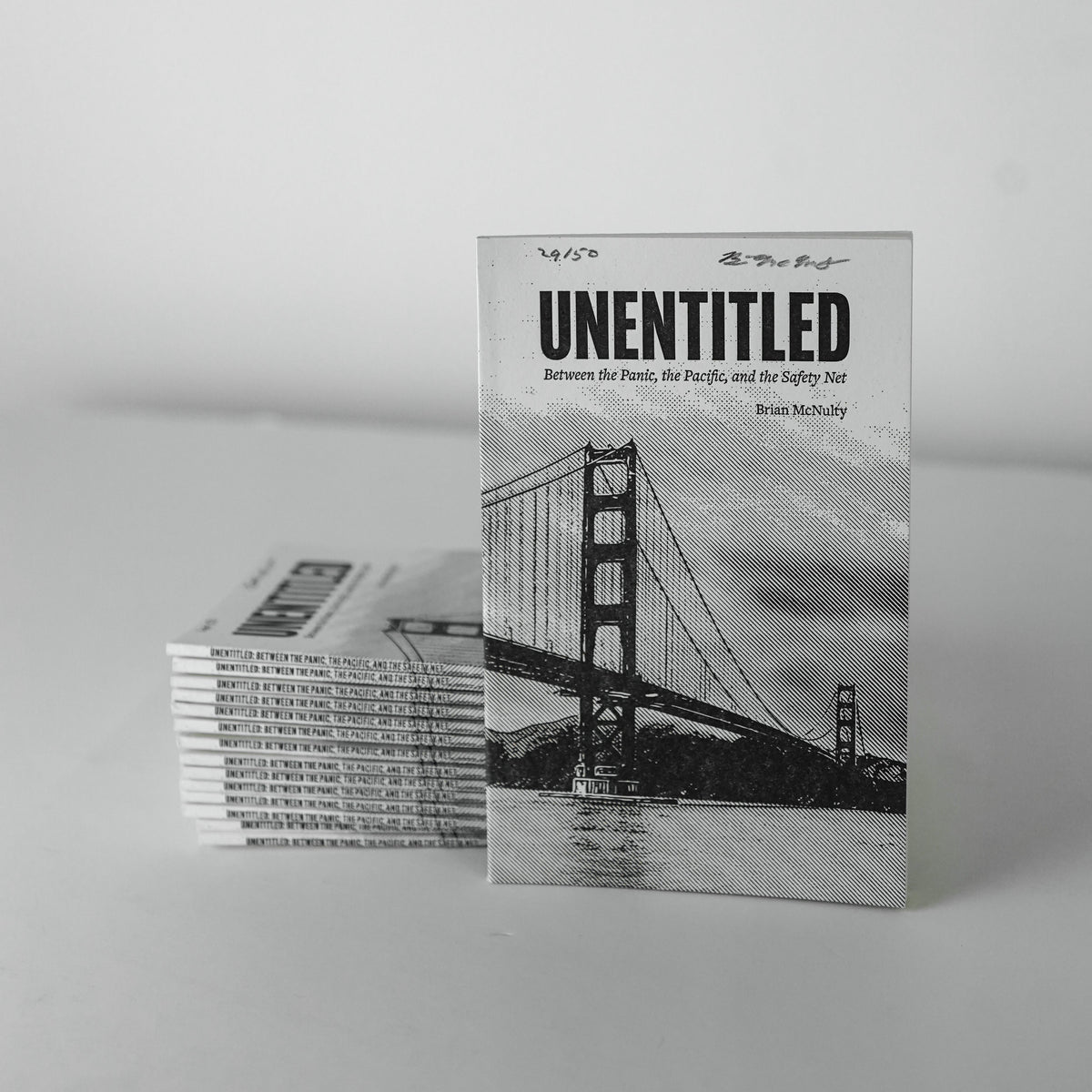 Stack of books titled 'UNENTITLED' with a black and white image of a bridge on the cover.